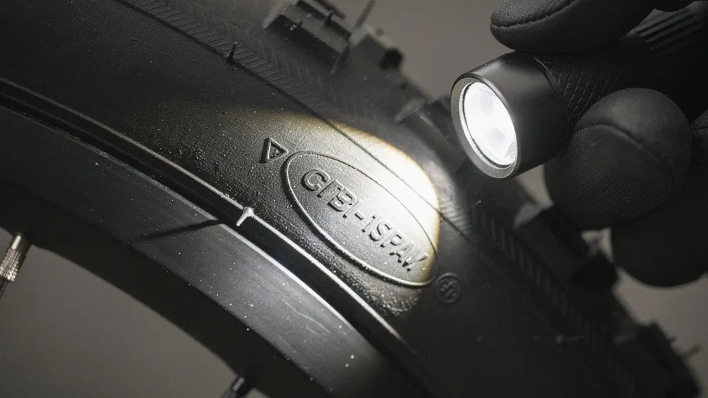 Close-up of an e-bike tire sidewall being inspected with a flashlight, with certification-style markings rendered out of focus and unreadable.