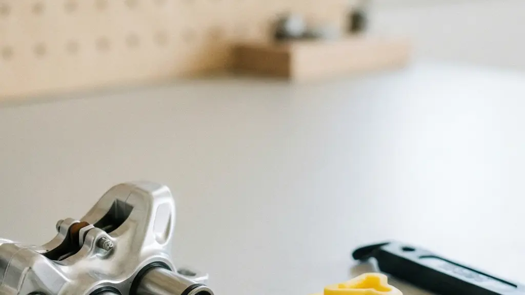 A bicycle brake caliper removed from the frame resting on a clean workbench with pistons partially extended, workshop tools softly blurred in the background