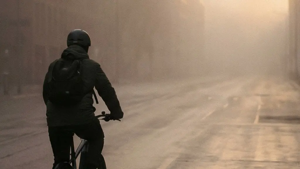 Solitary e-bike cyclist riding through a misty urban corridor at dawn, atmospheric haze softening the background buildings, emphasizing air quality concerns